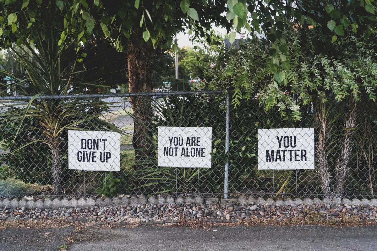 Three white posters on a chain-link fence reading, Dont give up, You are not alone, and You matter.